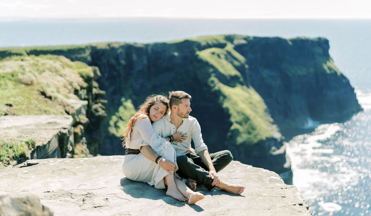 Britton and Carolee sitting together on a cliff overlooking the sea