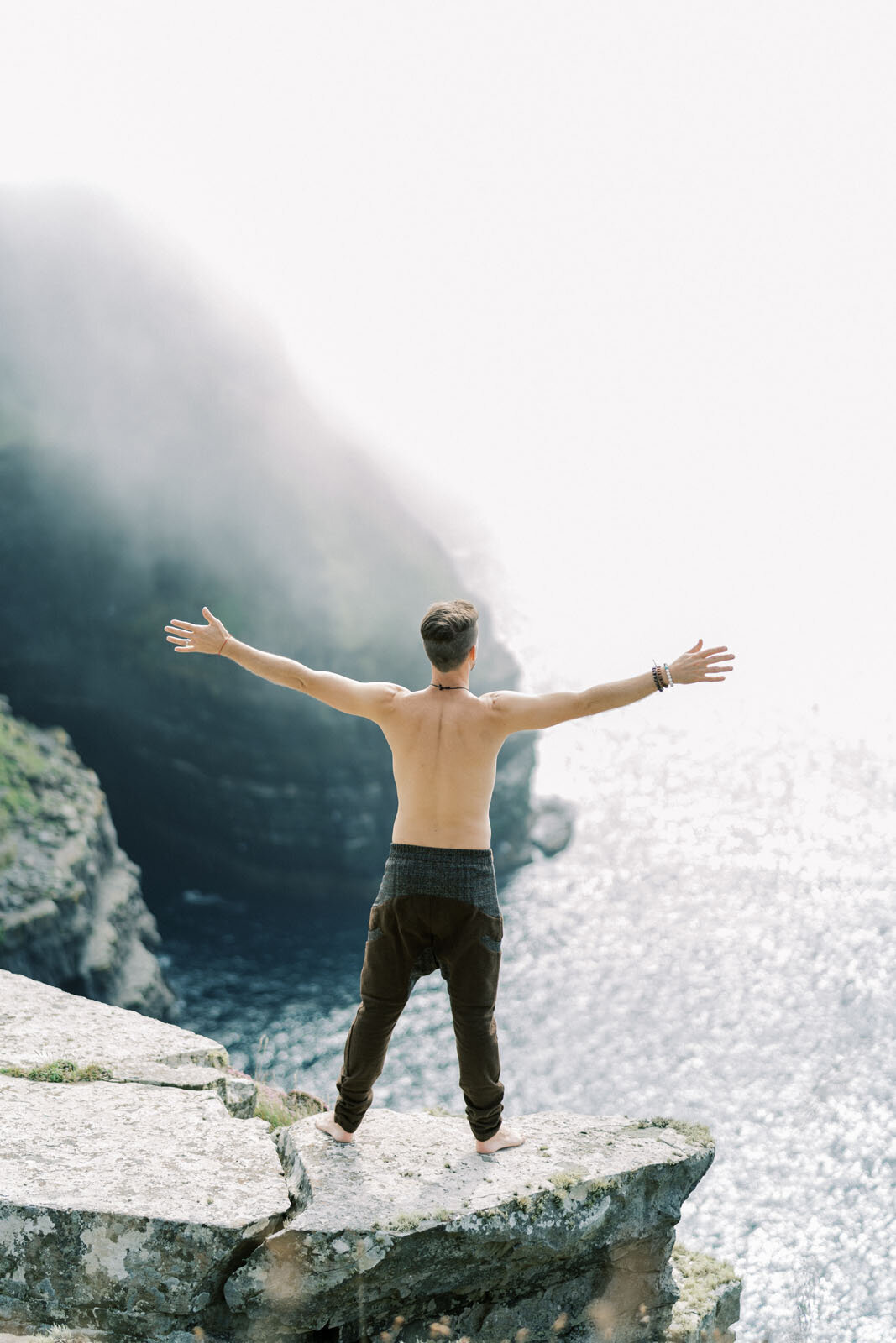 Britton standing on a cliff with arms open to the sea
